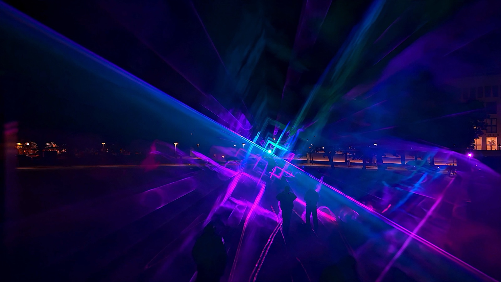 Visitors standing inside ÆTHER, a walk-in installation of green, magenta and blue light beams in fog at the Marx-Engels-Forum in Berlin