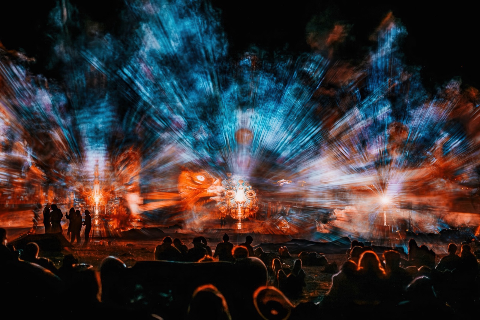 A crowd at night in front of three fan-shaped screens of water and fog on which giant blue faces of light appear — BEYOND by RE:SORB at Boom Festival