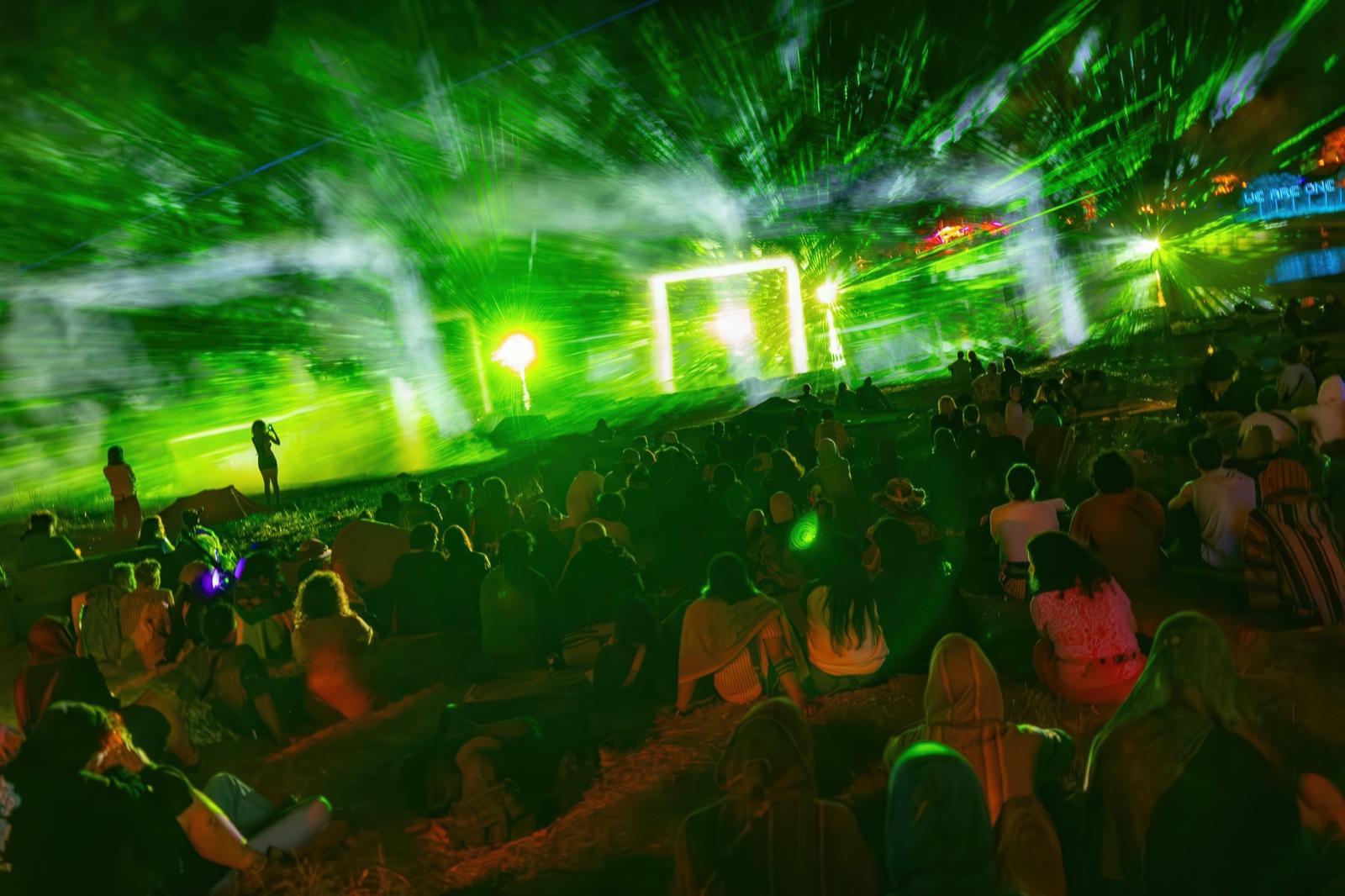 A crowd at night in front of three fan-shaped screens of water and fog on which giant blue faces of light appear — BEYOND by RE:SORB at Boom Festival
