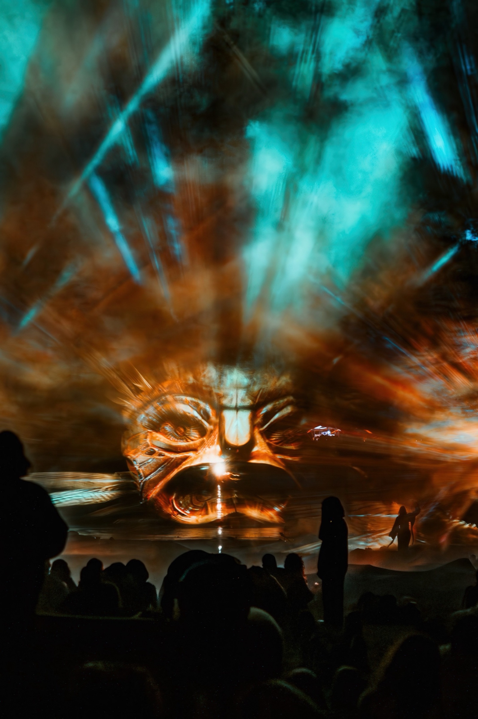 A crowd at night in front of three fan-shaped screens of water and fog on which giant blue faces of light appear — BEYOND by RE:SORB at Boom Festival