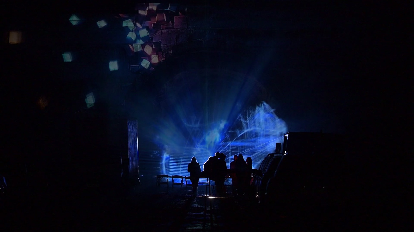 A stone railway tunnel portal in Tbilisi covered in a projection mapping of coloured tiles, with a hologram of light appearing in the tunnel mouth