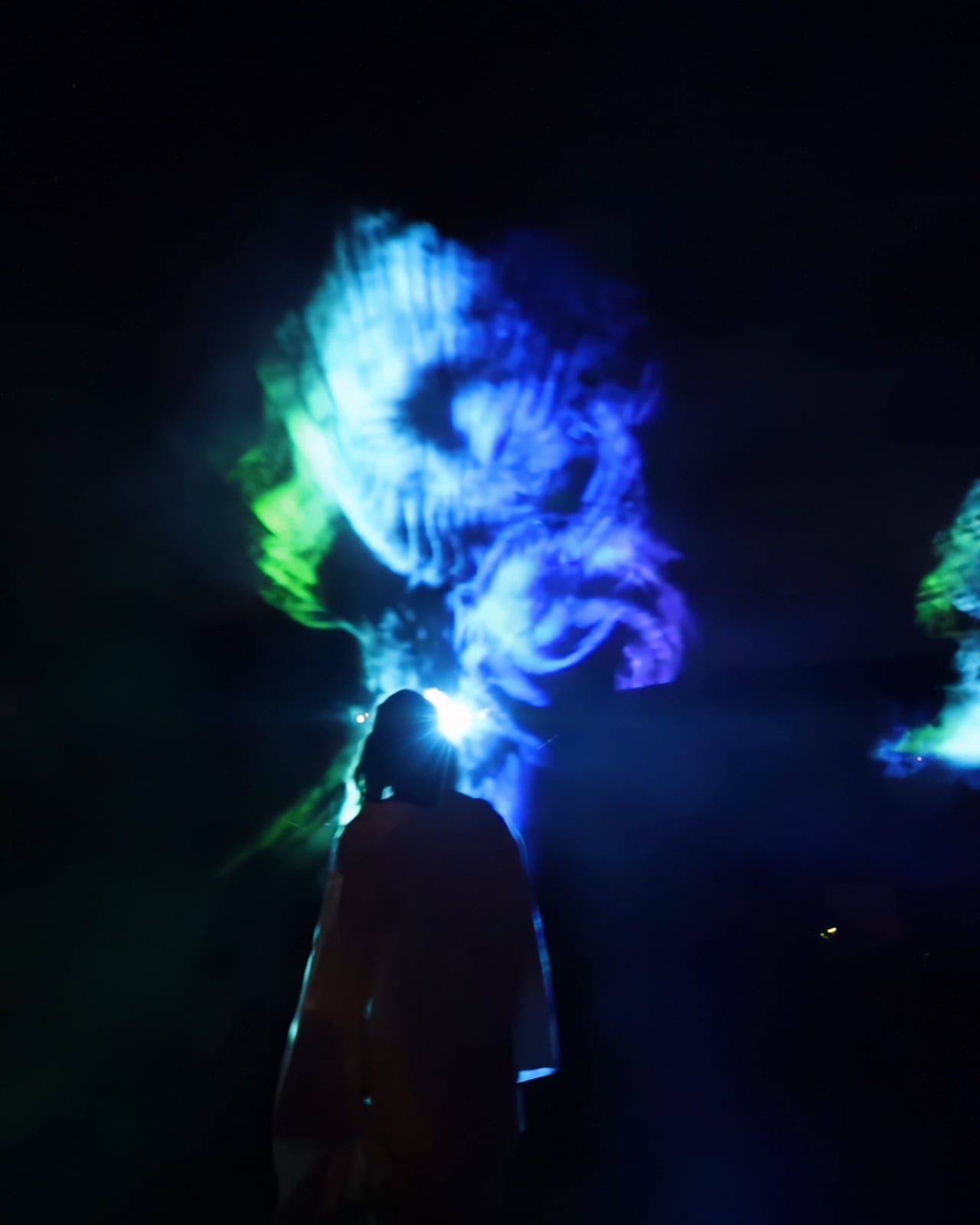 A visitor standing in front of a floating holographic figure of light in the dark at Boom Festival