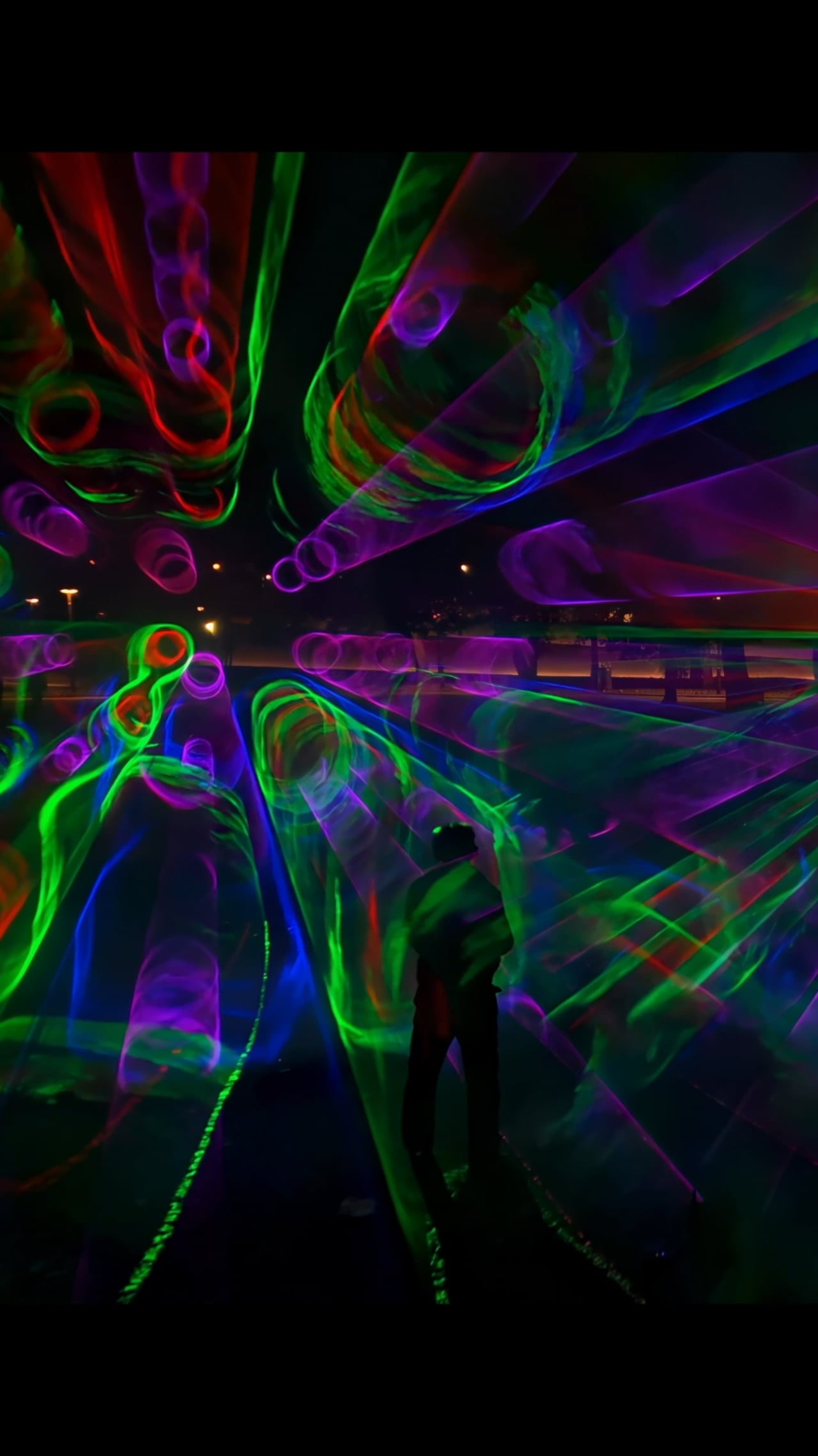 Swirling beams of pink, green and blue light in fog forming a walk-in space at the Marx-Engels-Forum, Berlin, filmed in vertical format