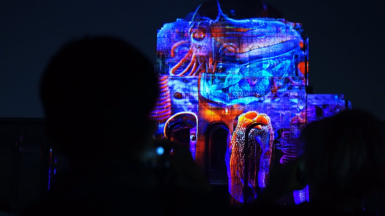 A building façade in Tokyo covered in organic blue and purple projection-mapped forms resembling living cells