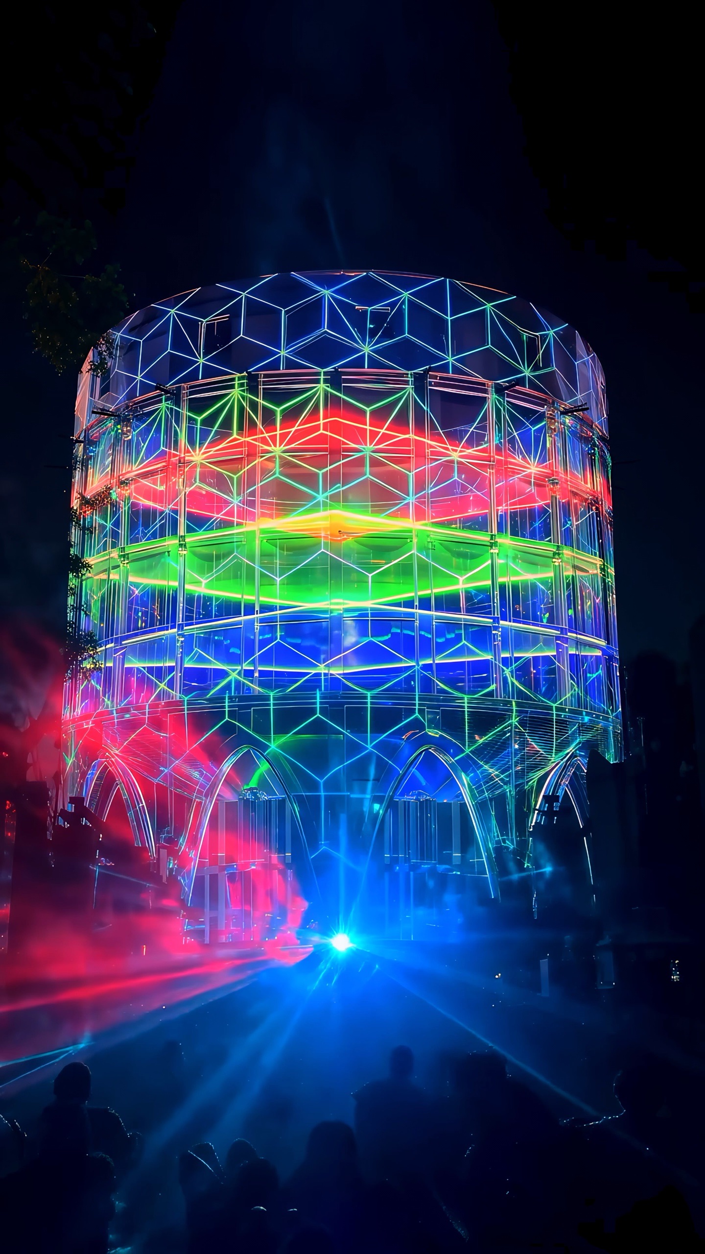 The 24-metre concrete silo of the Alembic Glass Factory in Bengaluru rendered as a transparent lattice by projection, with an amber interior glowing inside and holographic fog around it