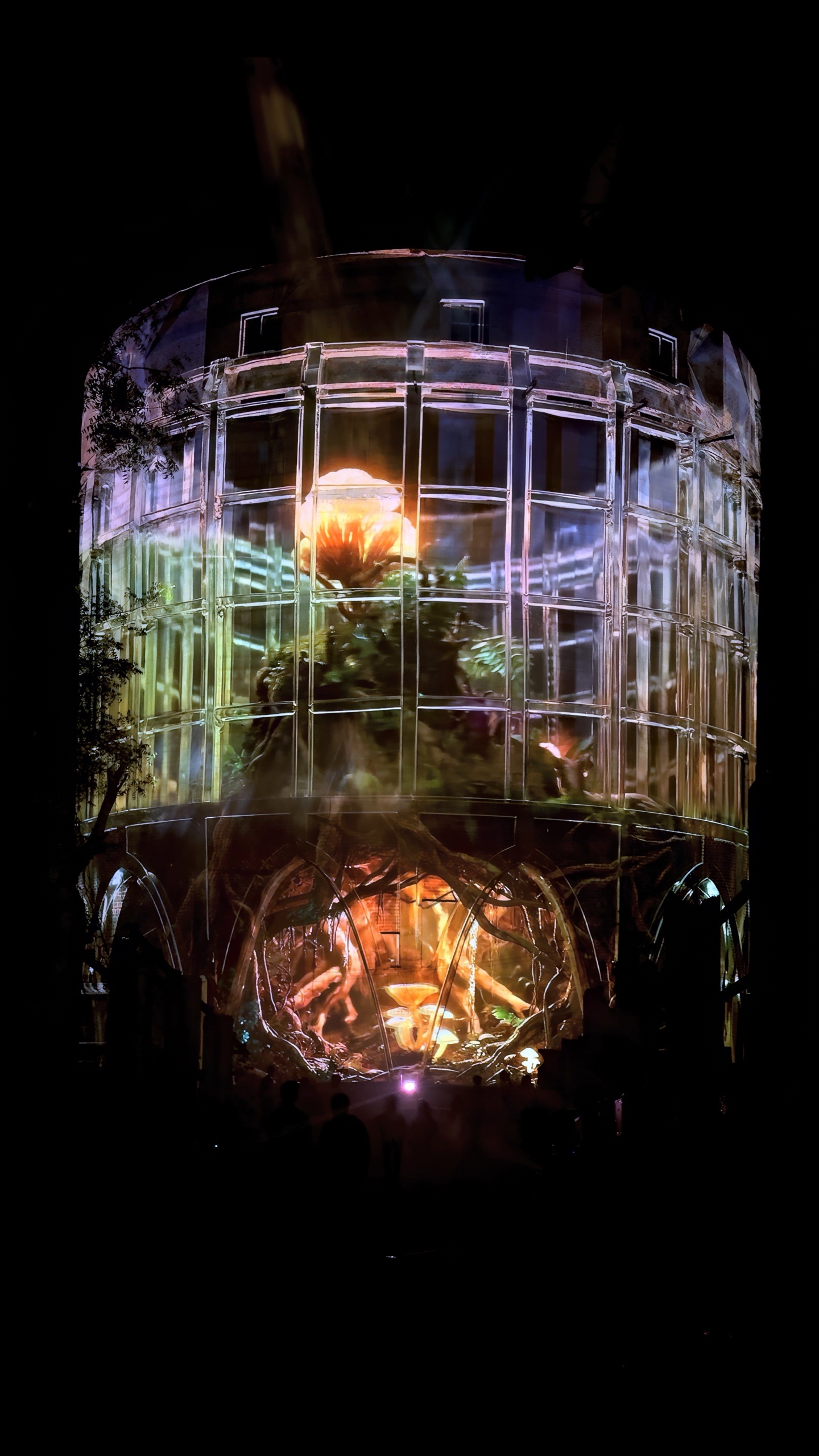 The 24-metre concrete silo of the Alembic Glass Factory in Bengaluru rendered as a transparent lattice by projection, with an amber interior glowing inside and holographic fog around it