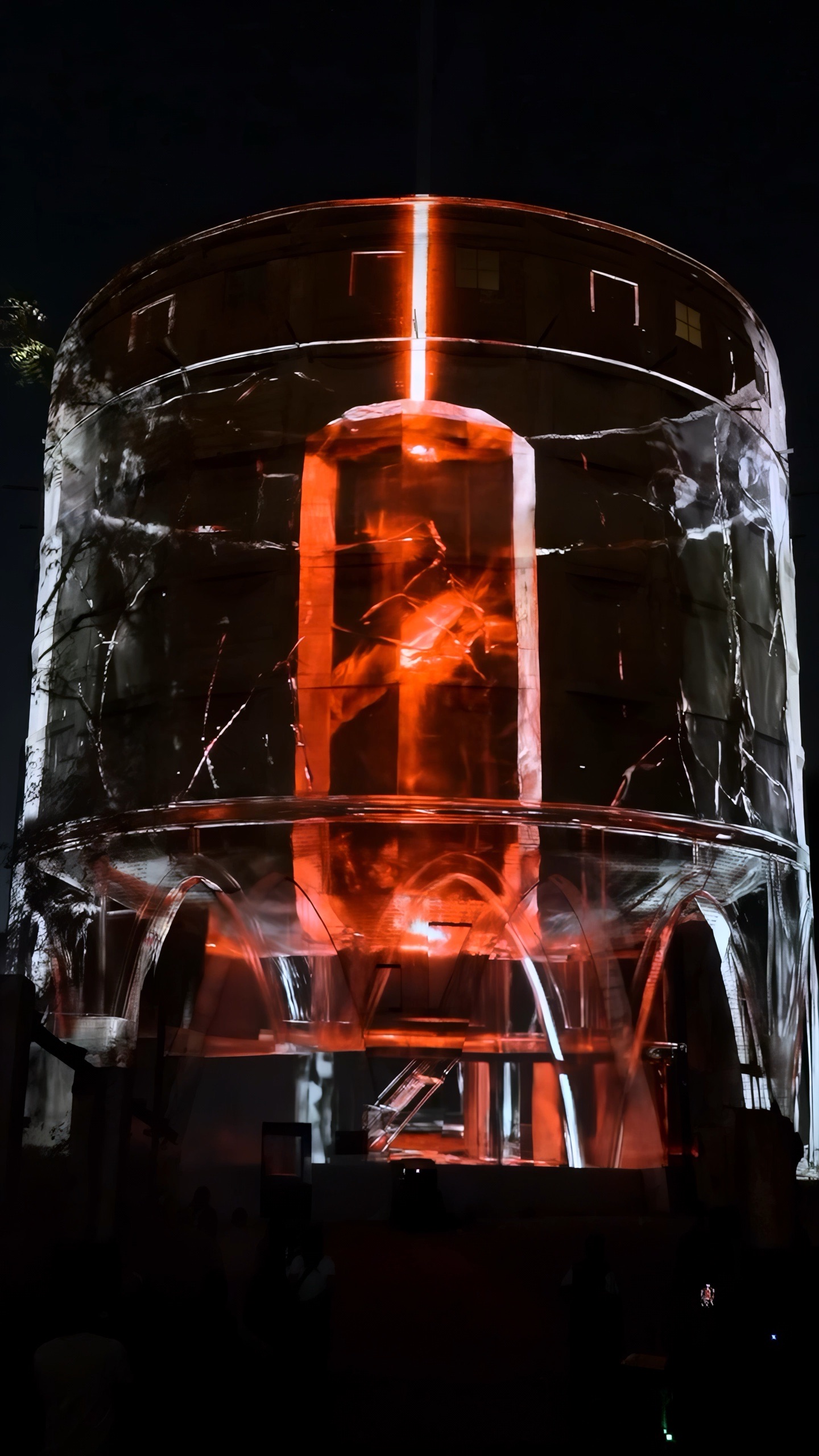 The 24-metre concrete silo of the Alembic Glass Factory in Bengaluru rendered as a transparent lattice by projection, with an amber interior glowing inside and holographic fog around it