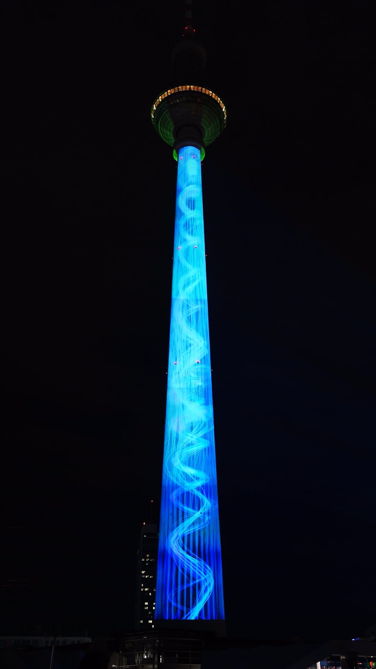 The Berlin TV Tower at night with its shaft and sphere illuminated in blue by a projection mapping, filmed in vertical format