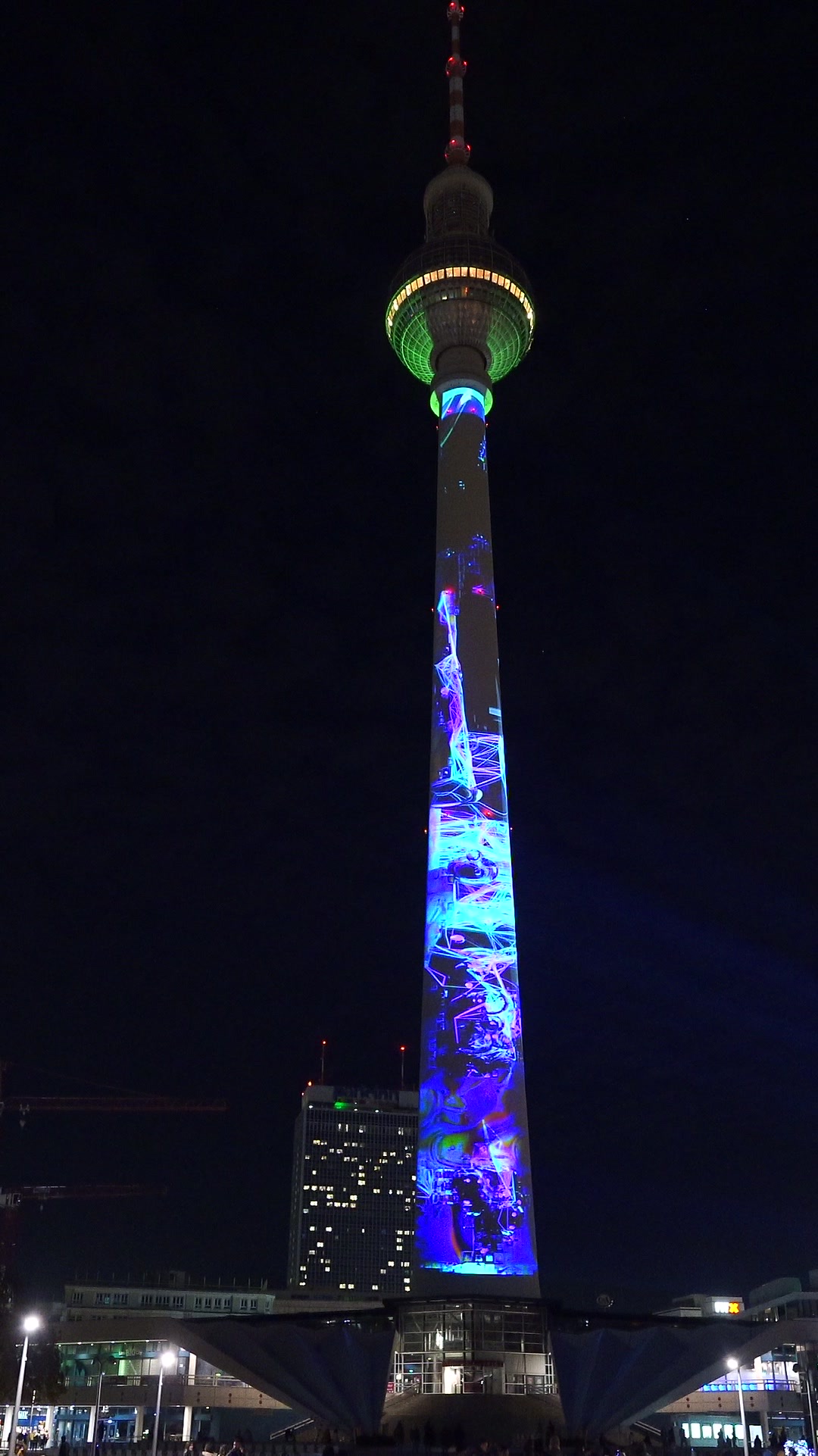The Berlin TV Tower at night with its shaft and sphere illuminated in blue by a projection mapping, filmed in vertical format