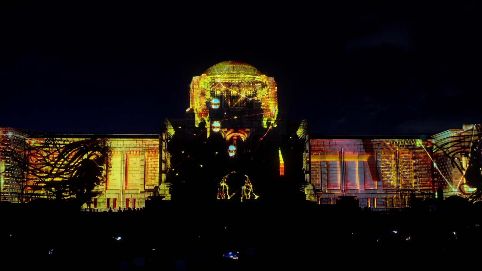 A façade in Tokyo lit by a projection mapping in which a giant face emerges from golden light